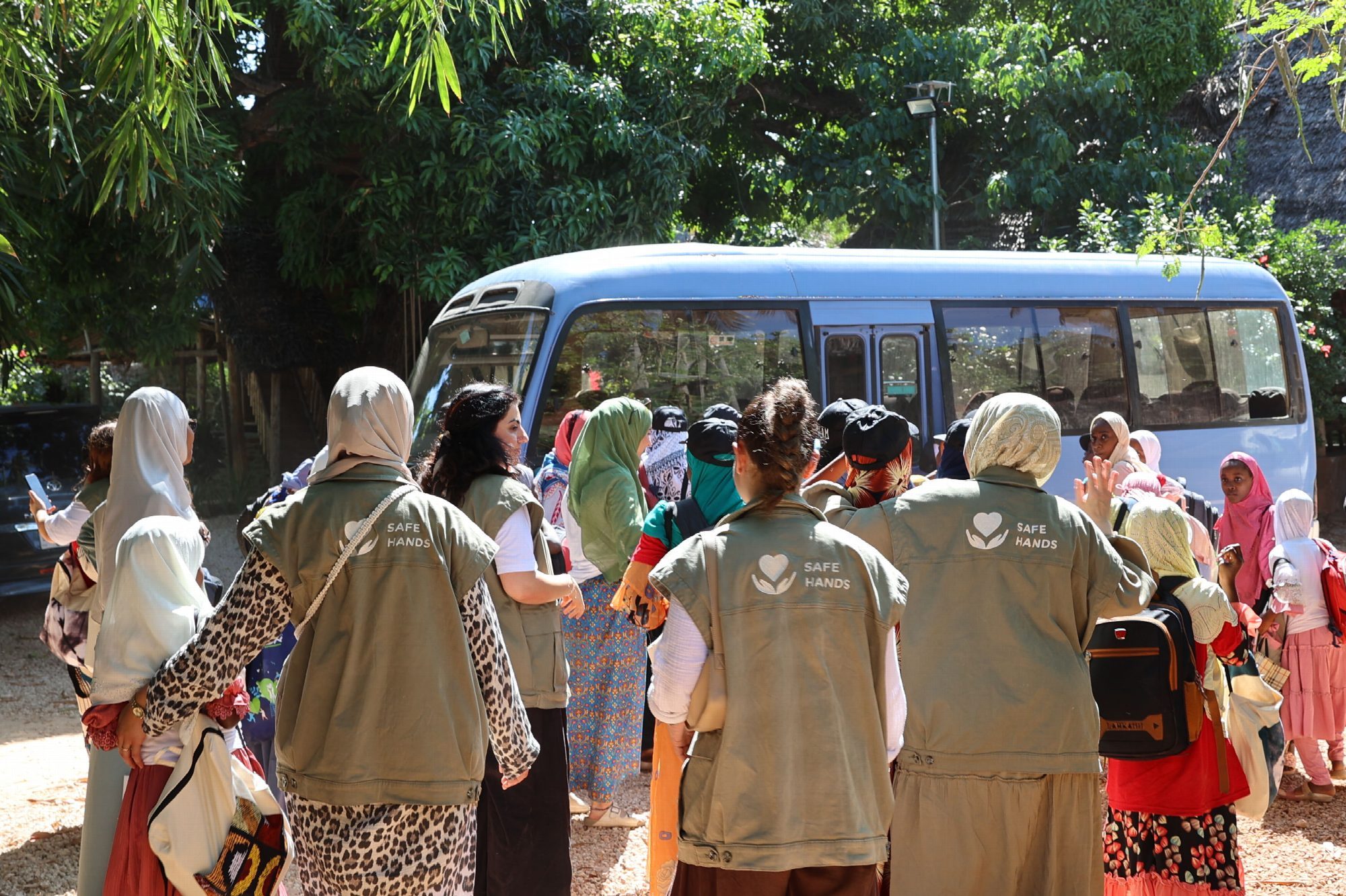 Mitarbeiterinnen in Vereinswesten vor einem Kleinbus, umringt von Kindern